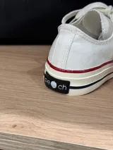 Zapatillas bajas de lona color blanco, con cordones marrones, puntera de goma y base blanca.