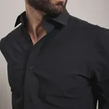 Camisa de vestir negra de manga larga, confeccionada en tejido técnico elástico y libre de arrugas, con cuello clásico y cierre frontal de botones.
