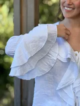 Camisa de lino azul marino con volados en cascada a lo largo del frente y en los puños de las mangas largas. Presenta un escote en V con un botón de nácar visible.