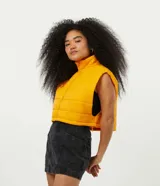 Chaleco cropped puffer color mostaza, con cuello alto y cierre frontal con cremallera.