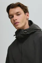 Campera rompevientos de nylon color verde oscuro, con capucha ajustable con cordón, cierre frontal y puños elásticos. Presenta bolsillos laterales y un bolsillo interior, todos con cierre.