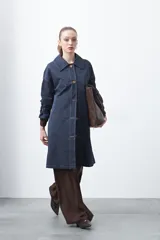 Trench de diseño clásico en color beige, con cierre frontal de botones, cinturón ajustable con hebilla a tono y mangas con trabillas en los puños.