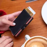 Billetera tipo tarjetero de cuero negro con caja de aluminio interna y sistema de deslizamiento para tarjetas. Cuenta con cierre mediante broche a presión.