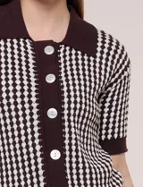 Cardigan de punto con patrón geométrico bicolor en gris y blanco, de manga corta, cuello polo y cierre frontal con botones nacarados.