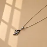 Conjunto de cadena y dije en plata 925. La cadena es de eslabones finos y el dije presenta un diseño orgánico con detalles texturizados y brillantes.