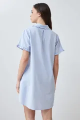 Vestido camisero corto color celeste melange, con cuello camisero y volados en el cuello, la tapeta de botones y los puños de las mangas cortas. Tiene un bolsillo de parche en el pecho.