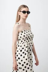 Vestido midi blanco con estampado de lunares negros, de silueta fluida con cuerpo fruncido, escote recto y tiras finas regulables. Presenta un corte bajo el busto que genera una caída suelta y liviana.