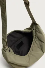 Bolso de hombro de nylon color negro, con diseño curvo y cierre de cremallera en el compartimento principal. Cuenta con asa ajustable para llevar al hombro y bolsillo interior con cierre.