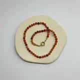 Collar de cuentas esféricas de cornalina de 6 mm, con cierre de mosquetón circular bañado en oro y detalles de nudos en hilo naranja.