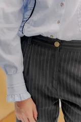 Pantalón sastrero de tiro medio, color gris oscuro con rayas verticales finas. Presenta pinzas delanteras, bolsillos delanteros con pin bordado y bolsillos traseros tipo vivo.