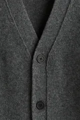 Cárdigan de punto fino color gris oscuro, con cuello en V pronunciado y cierre frontal de botones. Presenta un acabado ligeramente cepillado y puños y bajo acanalados.