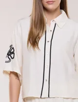 Conjunto de dos piezas negro compuesto por camisa de manga corta con cuello camisero y pantalón palazzo de tiro alto. Presenta detalles de bordados florales en contraste a lo largo de los laterales del pantalón y en las mangas.