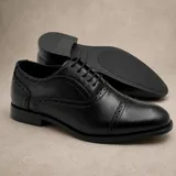 Zapato tipo Oxford de cuero sintético negro, con detalle de perforaciones decorativas tipo brogue y puntera reforzada. Cuenta con cordones al tono y suela de goma antideslizante.