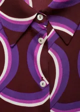 Camisa de tejido fluido color bordó con estampado geométrico abstracto en tonos morados y blancos, cuello camisero, manga larga y cierre frontal de botones.