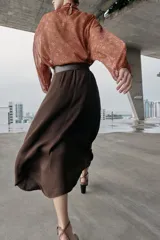 Camisa de estampado floral con cuello subido, lazo frontal y mangas largas con puños elásticos. Presenta un diseño con bajo asimétrico y cierre posterior con botones ocultos.