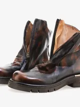 Bota corta de cuero bovino, color negro con efecto desgastado o metalizado grisáceo. Presenta cierre lateral con tirador y suela gruesa de goma con relieve.