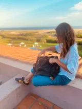 Mochila negra de cuero blando con herrajes dorados, correas marrones ajustables y cierre con cremallera.