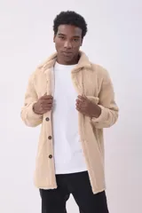 Cazadora de estilo camisa confeccionada en tejido de borreguillo color beige, con cierre frontal de botones, cuello clásico y bolsillo de parche en el pecho.