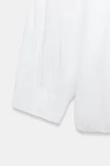 Camisa de algodón con cuello solapa, mangas abullonadas por debajo del codo y bajo acabado en globo. Presenta cierre frontal con botones ocultos.