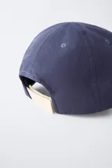 Gorra de béisbol azul marino con visera curva y detalle de borde en color crema. Presenta un bordado frontal con la palabra 'LONDON' en tipografía estilo varsity y texto adicional debajo.