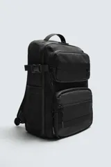 Mochila técnica de color negro con múltiples compartimentos, incluyendo dos bolsillos frontales con cierre, bolsillos laterales y compartimento principal acolchado para dispositivos electrónicos. Cuenta con parte posterior acolchada, banda de sujeción para equipaje, asa de mano y asas de hombro ajustables.
