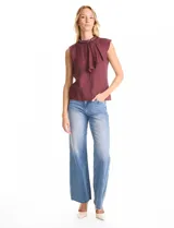 Blusa sin mangas color blanco, confeccionada en crepe con acabado satinado. Presenta un cuello alto decorado con mostacillas y una sobrecapa drapeada en el frente. La espalda cuenta con una abertura tipo gota y cierre de botón.