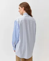 Camisa de corte recto y ligeramente oversize, confeccionada en algodón orgánico. Presenta un diseño a rayas con paneles en contraste de tonos azules y blancos, cuello clásico, cierre frontal de botones y un bolsillo en el pecho.