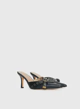 Mules de cuero negro con punta fina, diseño abierto en los laterales y tiras decorativas con ojales metálicos y hebilla ajustable.