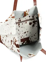 Cartera shopper confeccionada en cuero con pelo con estampado animal print tipo vaca en tonos blancos y marrones, con doble asa de hombro y bolsillo interior con cierre.