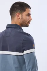 Remera polo de manga larga con diseño de bloques de color horizontales en tonos azul, verde y marrón. Presenta cuello clásico, cierre frontal con botones y bordado en el pecho. Cuenta con puños elásticos acanalados.