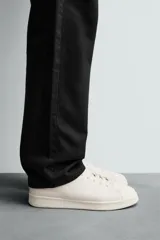 Zapatilla de cordones confeccionada en piel, con horma redonda y suela a tono. Presenta un diseño minimalista con detalle de contraste en el borde del talón.