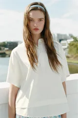 Camiseta blanca de algodón con cuello solapa, manga corta y cierre frontal con botones. Presenta un diseño regular fit con bajo acabado en tejido combinado a tono.