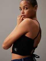 Top negro de denim rígido con cuello halter, diseño entallado y cropped, costuras moldeadoras en el pecho, espalda abierta con cierre anudado y logo de Calvin Klein en el bajo.