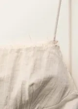 Vestido corto color crema, de breteles finos, escote recto con detalle de flecos y espalda descubierta.