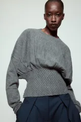 Jersey de punto color gris, con cuello redondo, manga larga y detalle de cintura ajustada con tejido tipo nido de abeja.