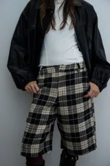 Bermuda de corte sastrero con diseño de cuadros escoceses en tonos beige y negro, de tiro alto y largo por debajo de la rodilla.