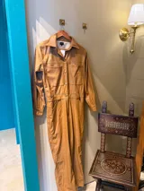 Mono largo color marrón con textura croco, cuello camisero, cierre frontal con botones, bolsillos en el pecho y cinturón a la altura de la cintura.