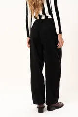 Pantalón de tiro medio con silueta curvada, más ancha en la zona de los muslos y rodillas, con cierre frontal de cremallera y botón.