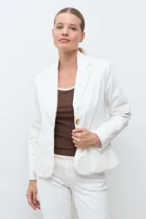 Blazer de pana color crudo, con solapas clásicas, cierre frontal de dos botones y bolsillos laterales. Diseño entallado con textura acanalada.