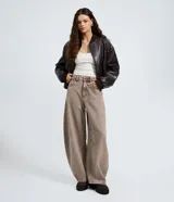 Pantalón de jean con corte barrel, de cintura alta y diseño de piernas anchas con volumen redondeado. Presenta bolsillos funcionales, trabillas para cinturón y cierre frontal con botón y cremallera.