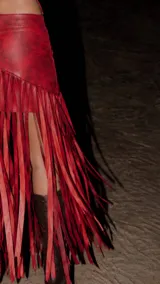 Pollera corta de cuero rojo con efecto marmolado, diseño asimétrico y larga cascada de flecos colgantes.