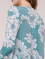 Blusa de gasa texturizada color verde con estampado floral blanco, cuello mao con escote en V y botones frontales. Cuenta con mangas 3/4 abullonadas y detalles de puntilla calada en el pecho.
