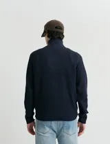 Remera de punto inglés con cuello alto y medio cierre metálico. Presenta mangas largas y puños en punto canalé.