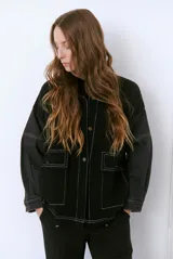 Campera color caramelo con mangas de denim azul oscuro. Presenta cuello alto, cierre frontal con botones, cuatro bolsillos delanteros con solapa y pespuntes blancos decorativos.