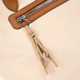 Bolso tipo tote color beige con detalles en marrón, cierre superior y bolsillo externo con cierre.