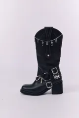 Botas de caña alta estilo western, confeccionadas en cuero negro. Presentan un diseño con costuras decorativas, detalle de arnés con hebillas metálicas y un taco cuadrado de altura media.
