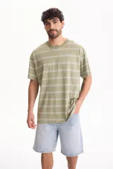 Remera oversize de manga corta confeccionada en 100% algodón, con diseño a rayas horizontales en tonos verde y blanco.