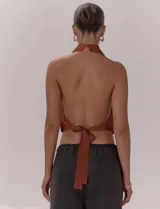 Top de escote halter con cuello alto, diseño frontal cruzado con pliegues y espalda descubierta con lazo regulable. Presenta una terminación elasticada en la cintura y está confeccionado en una tela liviana con caída fluida.