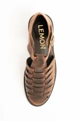 Sandalias cangrejeras de cuero color marrón, con diseño de tiras cruzadas y cierre de hebilla metálica en el lateral. Poseen suela plana y gruesa.