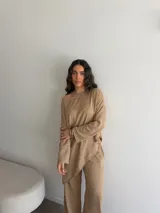 Conjunto de dos piezas color tostado, compuesto por una remera de manga larga con escote asimétrico y corte irregular, y un pantalón largo de corte recto y holgado.